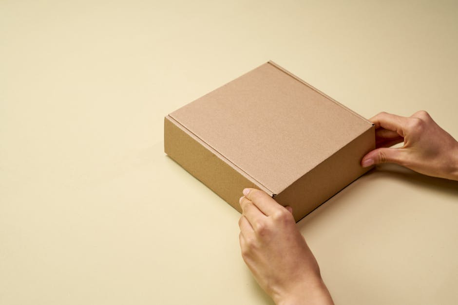 A close-up of hands opening a plain brown cardboard box on a beige surface, perfect for themes of shipping or packaging.tongue depressors